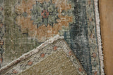 Sampler Oushak rug close-up: worn green, orange, blue pile, visible foundation, and fringe.