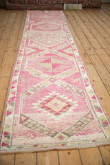 An angled, full-length view of a vintage distressed Kurd runner with a pink geometric medallion pattern.