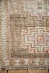 Distressed Kars rug's geometric border in sand, ivory, and faded magenta with fringe.
