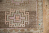 Distressed Kars rug detail: geometric hook-and-latch pattern in faded fuchsia, sand, and brown.