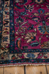Plush magenta pile, floral motifs in indigo and beige, with a patterned blue border and fringe.