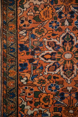 Vintage Hamadan rug detail: meandering border, floral field in burnt orange, blue, brown, showing knot wear.