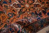 Rolled vintage Hamadan rug displaying textured pile, burnt orange, navy blue, and floral vine patterns.