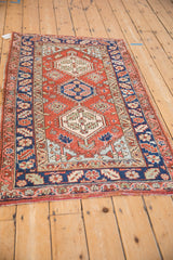 Angled view of a vintage Heriz rug showing its triple center medallion in red, navy, and ivory.