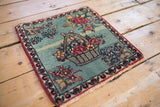 Angled perspective on an antique Kerman mat with a pictorial floral basket design.
