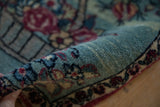A rolled corner of an antique Kerman mat reveals its plush, hand-knotted wool texture.