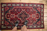 Vintage Persian Bijar rug shown for scale, with its detailed navy medallion on a red field.