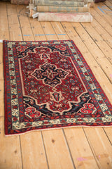 Vintage Persian Bijar rug with a navy medallion and red Herati field, viewed from an angle.