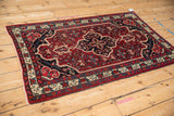 Angled view of a vintage Bijar rug's navy medallion and intricate red Herati field.
