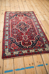 Angled view of a vintage Bijar rug showing its complete navy medallion and red Herati field design.