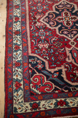 Intricate floral bouquet border and navy corner spandrel on a vintage hand-knotted Persian Bijar rug.