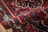 The dense, hand-knotted pile of a vintage Bijar rug, rolled to feature its red and navy floral border.