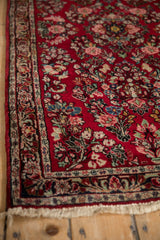 Angled view of a vintage Sarouk rug corner, showing the dense floral pile, border, and side selvage.