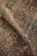 Soft, worn pile of a folded antique Kerman rug featuring red and ivory thousand flower motifs.
