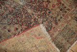 Storied antique Kerman rug with visible foundation, intricate floral motif, and tattered fringe.