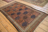 Corner of antique Belouch rug, showcasing madder red field, cobalt guls, and primitive vine border.