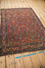 Angled view of an antique Bijar rug's detailed Samovar border and time-softened madder red Herati field.