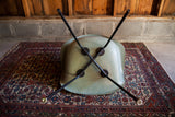 Black X-base of seafoam green Herman Miller chair with two brass-capped legs.