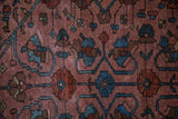 Sprawling indigo vines and floral blossoms on the dusty raspberry pile of an antique Lilihan rug.