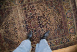 Antique Kermanshah rug with curvilinear medallion, dense floral field, and aged pile texture.