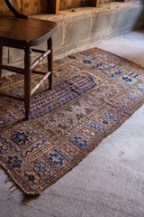 Nutty Brown Belouch prayer rug corner, showing geometric blue, purple motifs, and worn fringe.