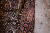Textured hand-knotted edge of a Belouch prayer rug with purple and brown pattern.