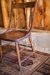 Antique oak chair legs with rustic patina and paint splatters, on a patterned rug.
