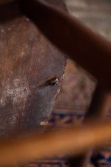 Detail of antique wooden chair's rustic texture, paint splatters, and secured bolt.
