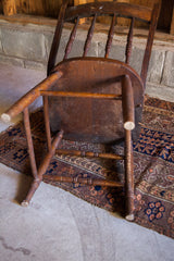 Underside view of an antique oak chair, showcasing rustic patina, spindles, and paint splatters.