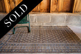 Tattered corner of an earthtone Caucasian rug showing repeating boteh on charcoal field.