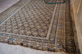 Earthtone Caucasian rug with charcoal field, tattered fringe, and geometric boteh pattern.