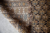 Close-up of repeating earthtone geometric motifs and tattered fringe on a Caucasian rug.