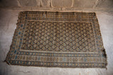 Earthtone Caucasian rug with geometric boteh, charcoal field, soft pile, and visible end wear.