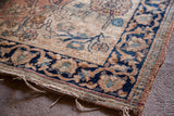 Blanched vintage Persian rug corner, showing dark blue floral border and tattered edge.