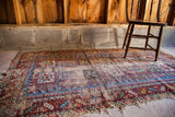 Tattered antique Caucasian rug, featuring bold geometric patterns and exposed foundation in red, blue.