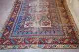 Intricate geometric patterns and brilliant colors of a tattered antique Caucasian rug with extensive wear.