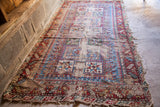 Antique Caucasian rug: geometric red and blue design, heavy wear, visible holes, exposed foundation.