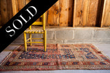 Worn antique Kazak prayer rug displaying faded red, blue, and beige geometric motifs.