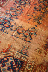 Antique Kazak rug close-up: faded geometric motifs in indigo, red, with prominent foundation.