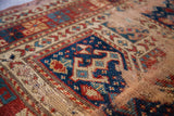 Worn geometric prayer motif in deep blue, red, and beige on an antique Kazak rug.