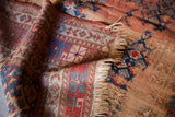 Antique Kazak rug fringe and worn geometric patterns in muted terracotta, blue hues.