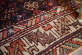 Detail of a vintage tribal rug showing worn pile, geometric patterns, and rich warming colors.
