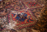 Textured detail of the worn geometric tribal rug, with vivid red and blue patterns over a visible foundation.