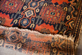 Tattered fringe, exposed foundation, and dark geometric motifs of an antique Persian Senneh rug.