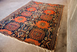 Corner of antique Persian Senneh rug, showing heavy tattered ends and rust geometric motifs.