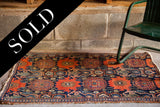 Worn antique Senneh rug, featuring tattered ends and unique rust and navy Damask-style patterns.