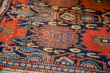 Antique Persian Senneh rug segment showing geometric motifs in deep blue, rust, and tan.