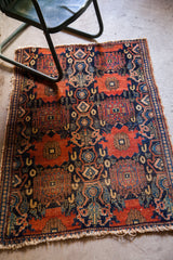 Dark navy and terracotta geometric pattern on an antique Senneh rug, showing tattered fringe.