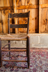 Antique rush seat chair's dark wood legs, aged patina, and undone woven seat.