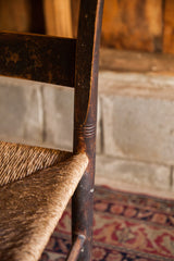 Antique chair with aged dark wood frame and detailed grooving above natural woven rush seat.